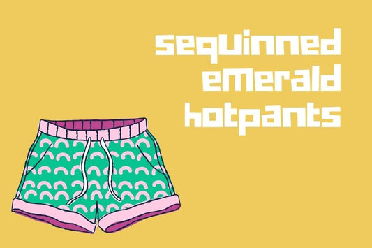 A pair of green cartoon hotpants with pink rainbows against a yellow background. Text reads: sequinned emerald hotpants